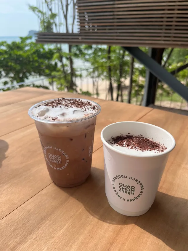 Two iced J&O cacao drinks on a wooden table overlooking the beach